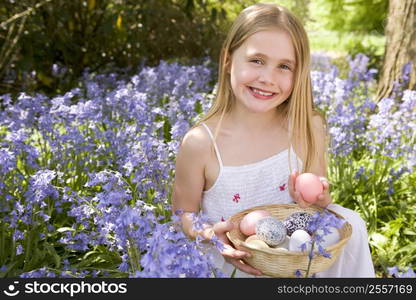 Young girl outdoors holding various eggs in basket smiling