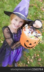 Young girl outdoors in witch costume on Halloween holding candy