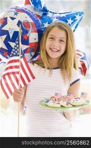 Young girl outdoors on fourth of July with flag and cookies smiling