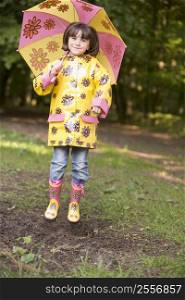 Young girl outdoors with umbrella jumping and smiling