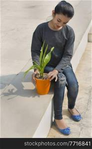 Young girl planting a small plant in a flower pot sitting on steps on a sunny day.
