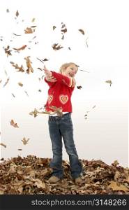 Young girl playing in dried leaves.