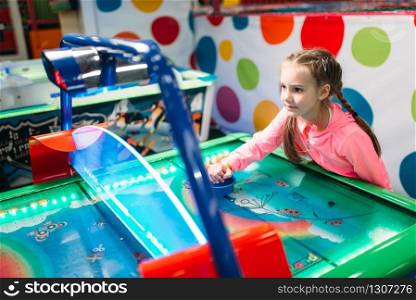 Young girl plays air hockey in entertainment center. Happy childhood. Sport game attraction