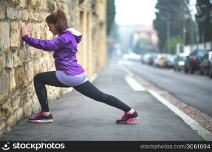 Young girl practices stretching in the city on a wall of a building