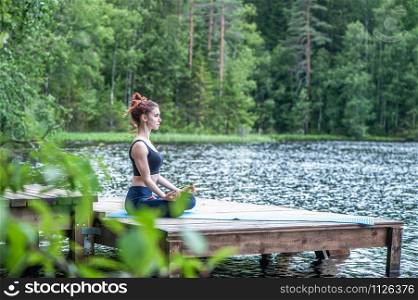 Young girl practicing yoga in the nature on the lake. Female happiness. Landscape background