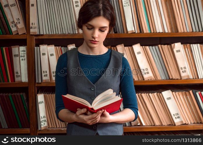 Young girl reading a book. Bookshelf with books and textbooks on the background.