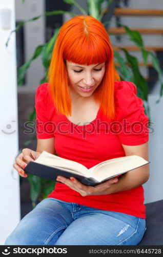 Young girl reading a book on the sofa at home