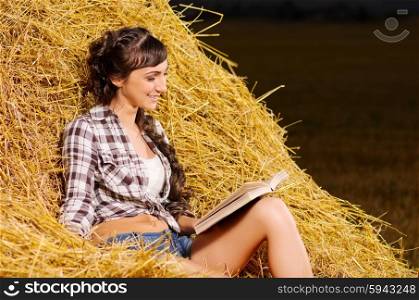 Young girl reading book on haystack