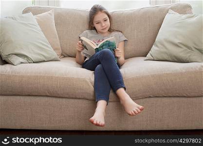 young girl reading book on sofa