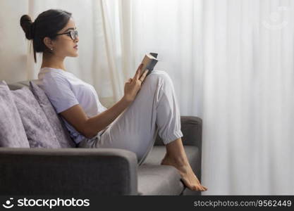 Young girl reading book while leaning on sofa