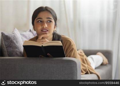 Young girl reading book while lying down on sofa