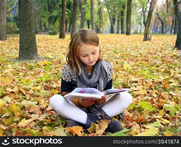 young girl reads a book in the autumn park. young girl reads a book in the autumn park lying on the ground