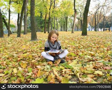 young girl reads a book in the autumn park. young girl reads a book in the autumn park sitting on the ground