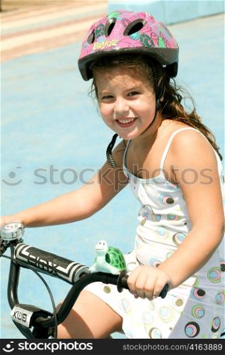 Young girl riding bicycle with safety helmet on looking at camera