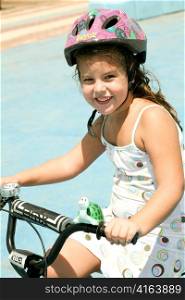 Young girl riding bicycle with safety helmet on looking at camera
