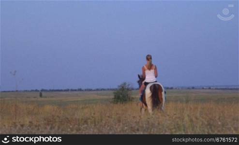 Young girl riding horse down the trail across the field