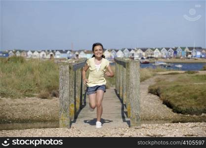 young girl running over foot bridge with beach huts in backgrounds
