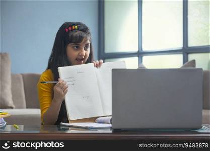 Young girl showing the spellings of the words her teacher dictated in front of the laptop during online class