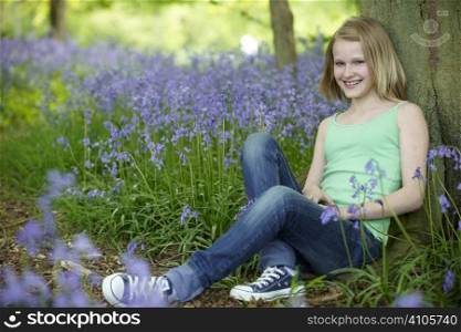 young girl sitting against a tree in a wood full of bluebells