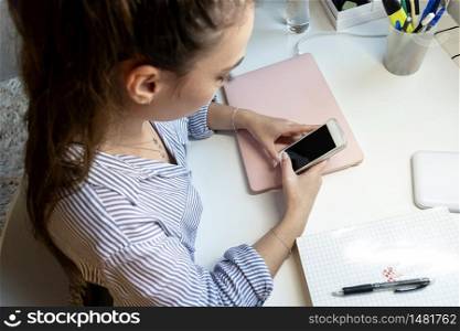 Young girl sitting at a laptop and using a smartphone.