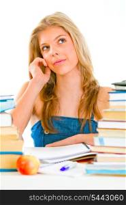Young girl sitting at table with books and dreamy looking in corner&#xA;