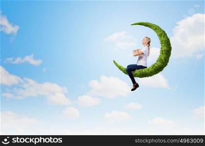 Young girl sitting on green moon high in sky. Woman on moon
