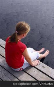 Young girl sitting on the edge of boat dock dipping her feet in water