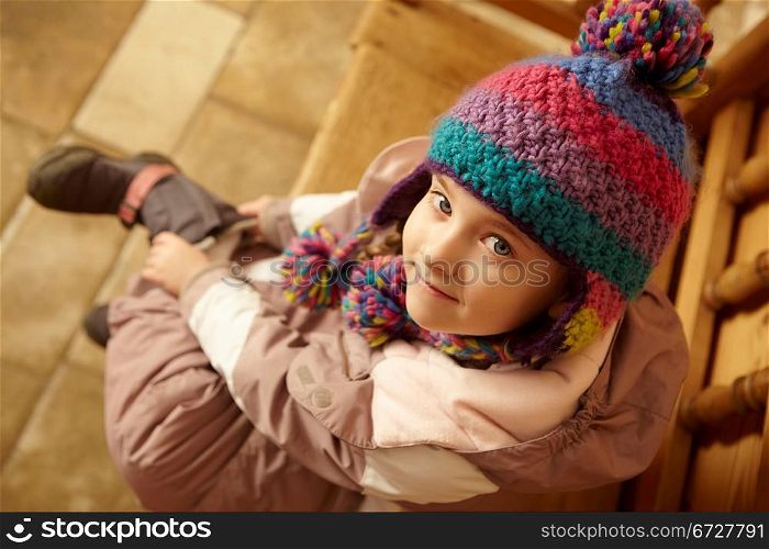 Young Girl Sitting On Wooden Seat Putting On Warm Outdoor Clothes And Boots