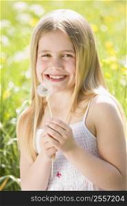 Young girl sitting outdoors holding dandelion head smiling