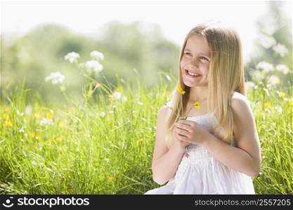 Young girl sitting outdoors holding flower smiling