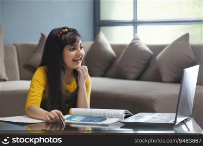 YOUNG GIRL SMILING WHILE ATTENDING AN ONLINE CLASS WITH BOOKS KEPT ON THE TABLE