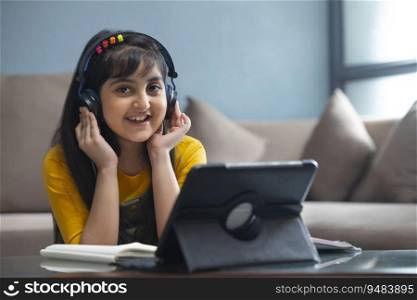Young girl smiling with her hands on headphones and sitting in front of a tablet