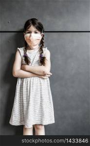 Young girl standing against a wall wearing a protective mask during Covid-19 pandemic.