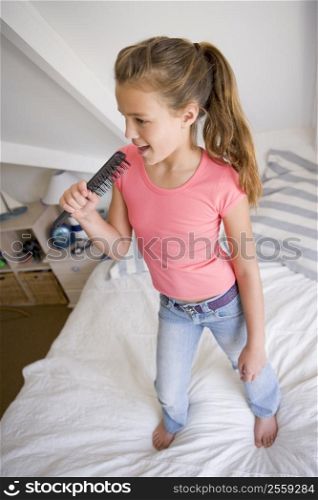 Young Girl Standing On Her Bed, Singing Into Her Hairbrush