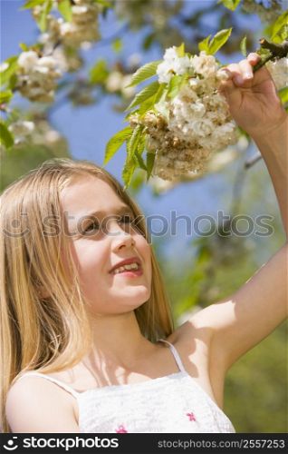 Young girl standing outdoors holding blossom smiling