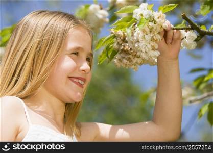 Young girl standing outdoors holding blossom smiling