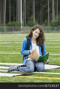 Young girl studying on soccer field with woods in background