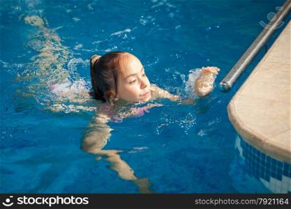 Young girl swimming to the edge of swimming pool