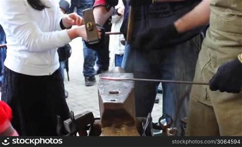 young girl takes big hammer and with blacksmith makes notches on metal rod, part1