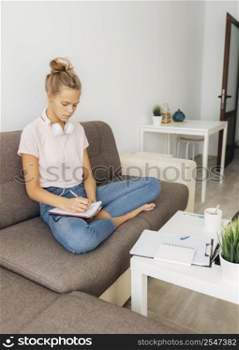 young girl taking notes from her online class