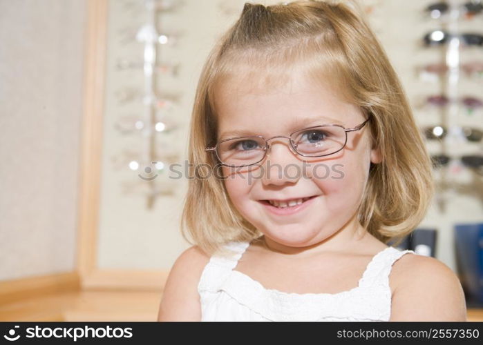 Young girl trying on eyeglasses at optometrists smiling