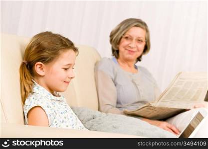 Young girl using computer laptop while grandmother read book at home