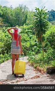 young girl walking down the road with yellow suitcase in the tropics