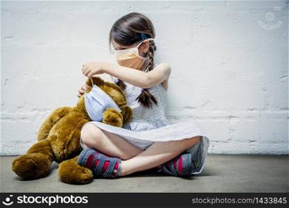 Young girl wearing a mask placing a mask on her teddy bear during covid-19 pandemic.