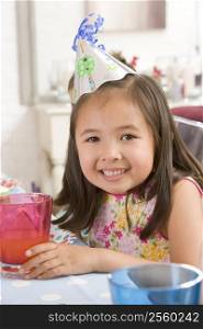Young girl wearing party hat at table smiling