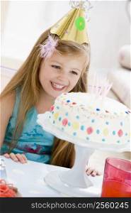 Young girl wearing party hat looking at birthday cake smiling