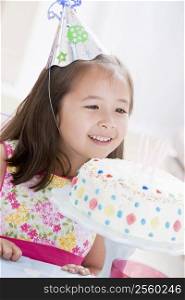 Young girl wearing party hat looking at birthday cake smiling