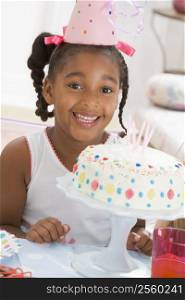 Young girl wearing party hat with cake in front of her smiling