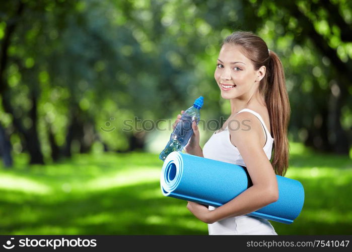 Young girl with a bottle of water and gym mat in the park