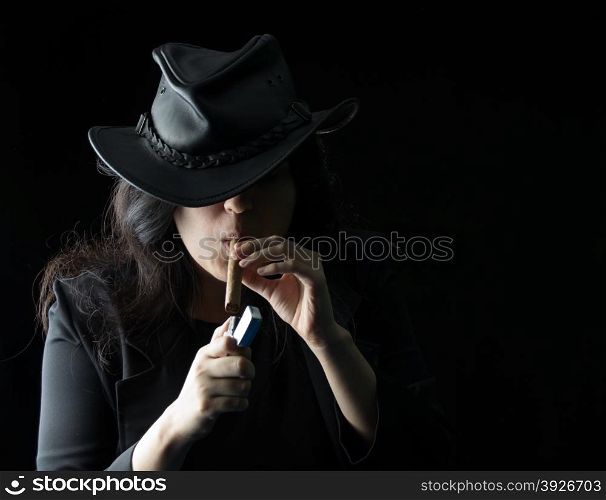 Young girl with a cigar in her mouth wearing black leather jacket and hat and holding a lighter up to the cigar